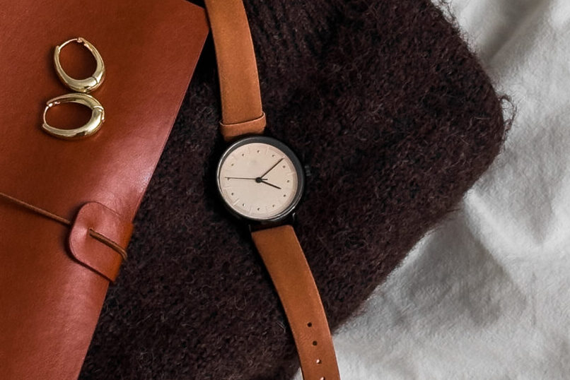 Women's brown cashmere sweater, leather-bound notebook, watch on a light background, top view